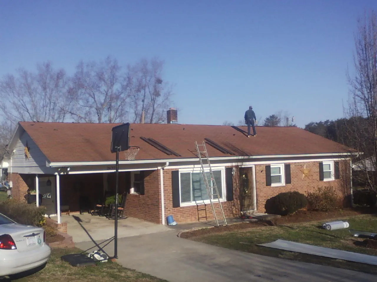 Roofer stripping a shingle roof on a brick ranch before metal panels in Darlington