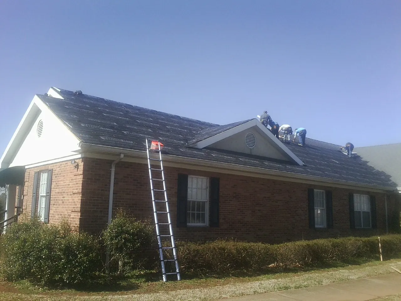 Crew tearing shingles off a brick ranch roof with a ladder set — Metal Roof Repair work by our crew in Darlington