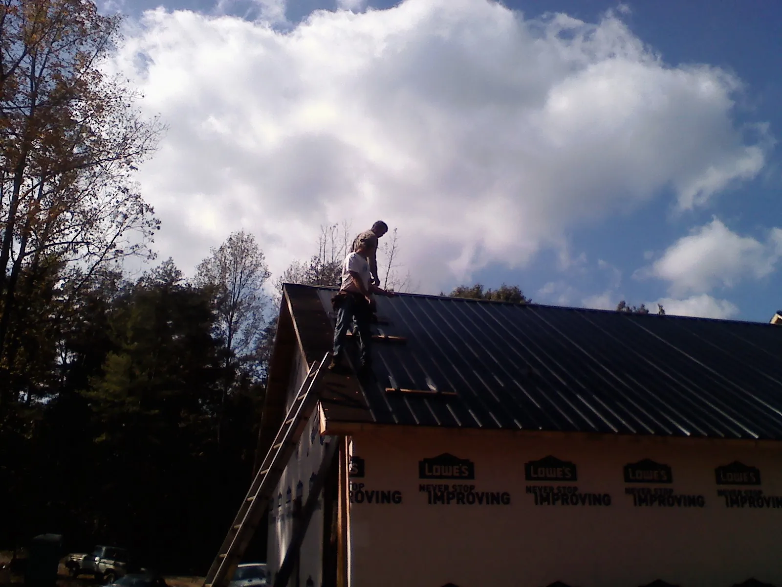 Roofer fastening dark metal panels high against a cloudy sky, from a Roof Inspection job in Darlington